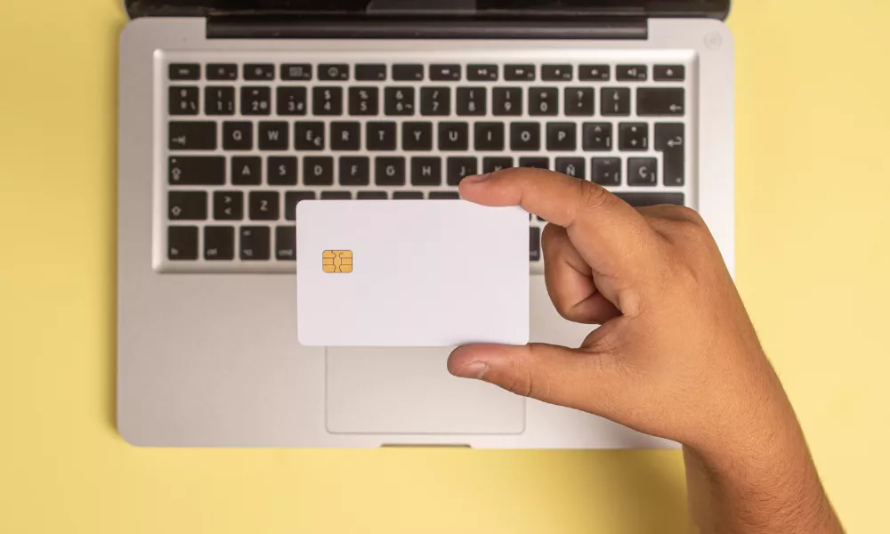 Hand holding a white card with a chip over a MacBook keyboard