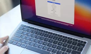 A person's hand is shown selecting the 'Sign Out' option in the iCloud settings on a MacBook Air screen.